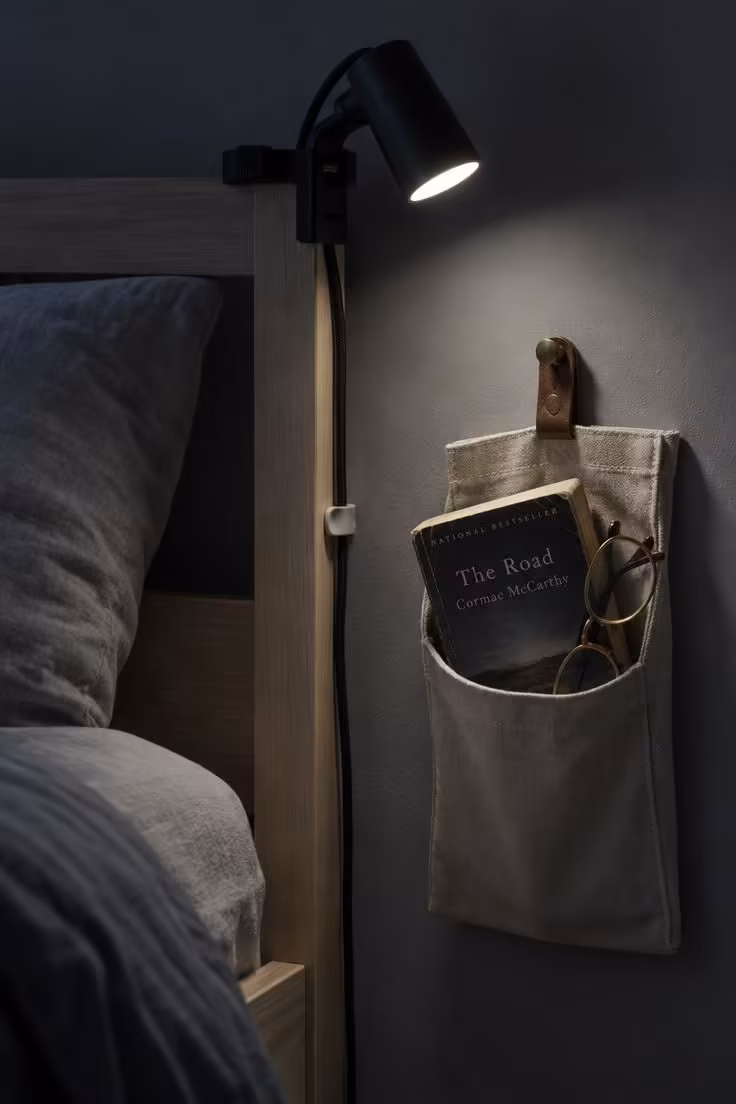 13 Cozy Small Bedroom Ideas for Teens to Love Today 10 Clamp-style reading light on a bed frame with a canvas wall pocket holding a paperback and glasses.