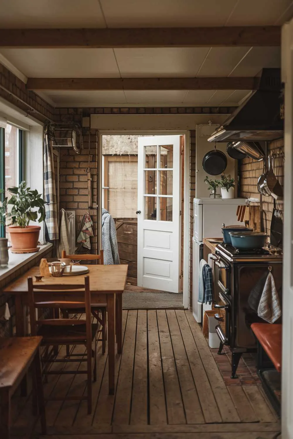 21 Small Farmhouse Kitchen Ideas for Country Style Comfort 2 A cozy small farmhouse kitchen with a wooden table, a few chairs, and a vintage stove. There are pots, pans, and utensils hanging on the wall. A potted plant is placed on the windowsill. The floor is made of wooden planks. The walls are made of bricks. There's a door leading outside. The room has a warm and rustic ambiance.