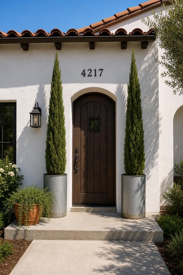 17 Cozy Small Front Yard Landscaping Ideas You Will Love 2 Dwarf Italian cypress trees in tall zinc cylinder planters flanking a white stucco front entry in bright midday light