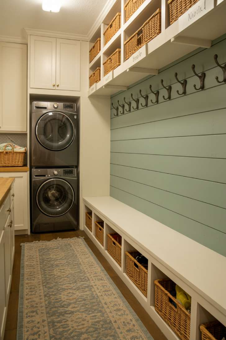 A narrow laundry-mudroom combination with stacked machines on one side and a built-in bench with coat hooks on the other