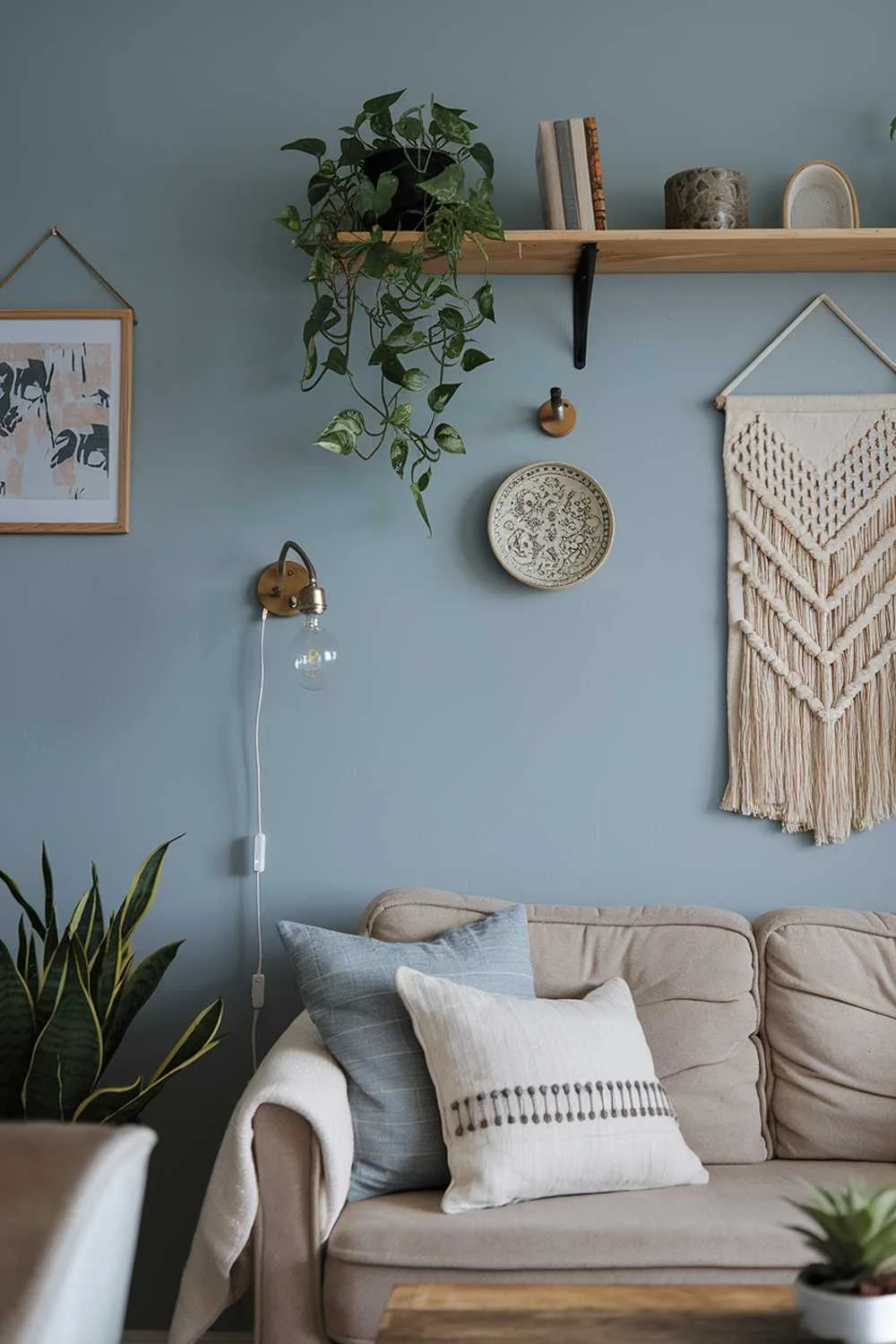 A cozy small Scandinavian living room decor. There is a beige sofa with a few pillows and a wooden coffee table. Above the sofa, there is a wall shelf with a few decorative items. There are also a potted plant and a vintage lamp. The walls are painted blue and have a few hanging items.