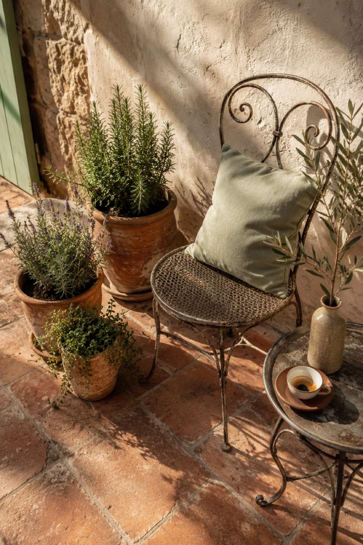 Small Mediterranean terrace corner with wrought-iron chair, terracotta herb pots and sun-bleached stucco wall in warm afternoon light
