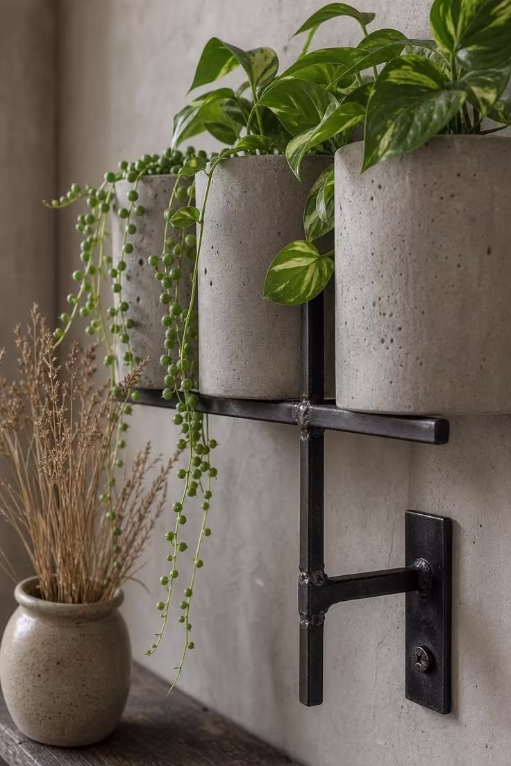 Concrete planters with trailing greenery on an iron wall bracket in a soft industrial interior