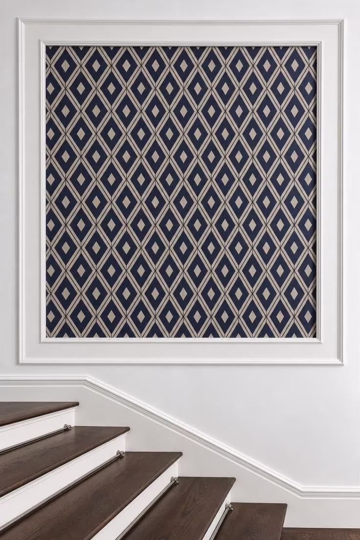 Navy and cream geometric wallpaper panel framed by white molding on a staircase wall