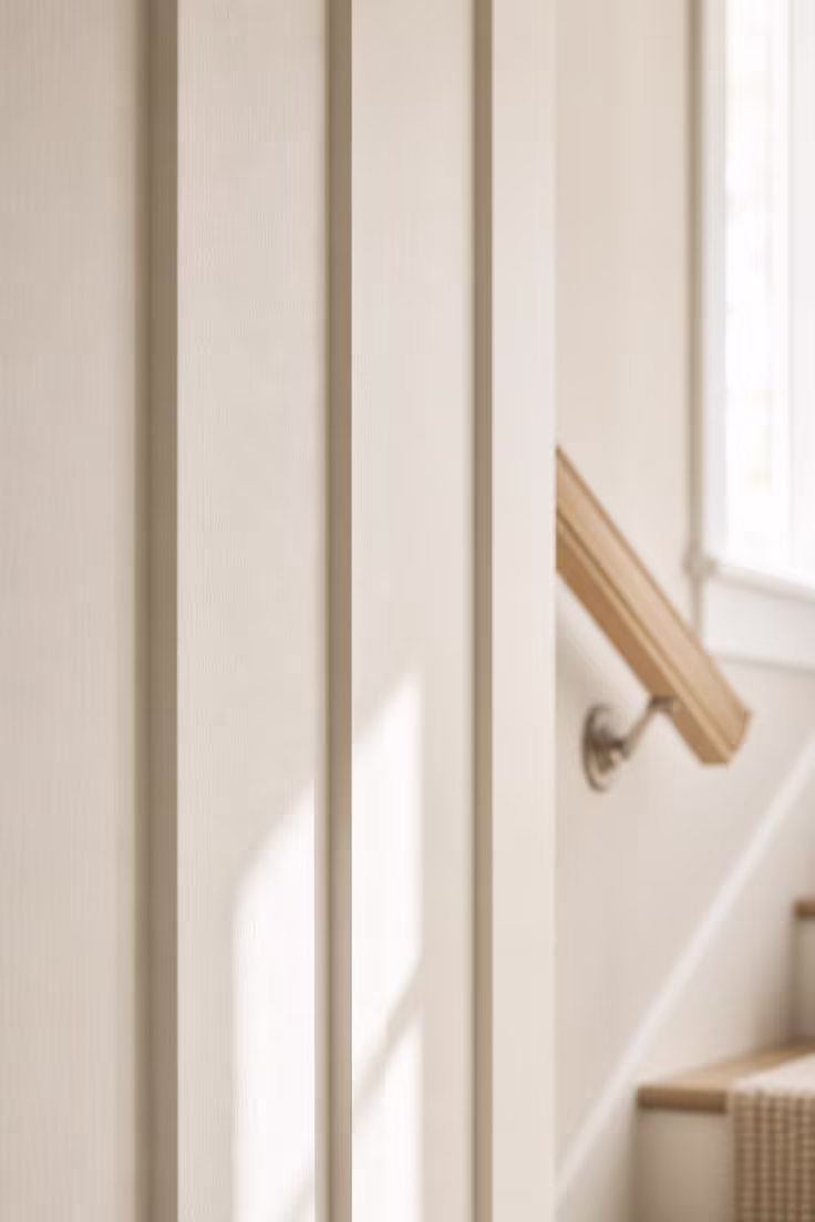 Close-up of creamy white board-and-batten paneling on a staircase wall with crisp shadow lines between battens