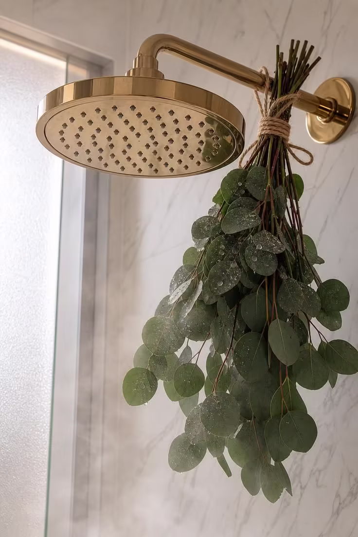 Fresh eucalyptus stems tied with jute twine to a brass rainfall showerhead with water droplets and soft diffused light