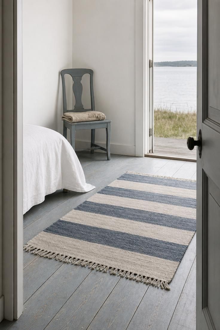 10 Breezy Summer House Bedroom Ideas For Slow Mornings 6 Wide pine floorboards painted Gustavian grey-blue with a cotton dhurrie rug and a glimpse of water beyond.
