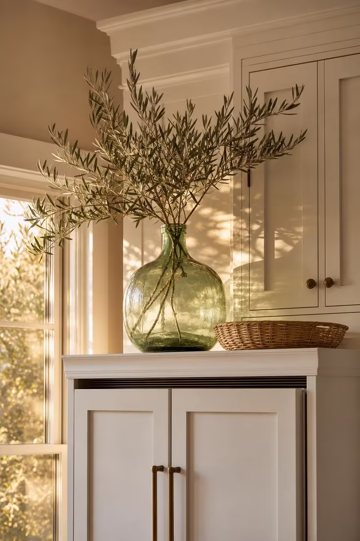 15 Bright Summer Kitchen Ideas to Refresh Your Space 15 A vintage green glass demijohn full of olive branches on top of a paneled refrigerator in warm afternoon light.