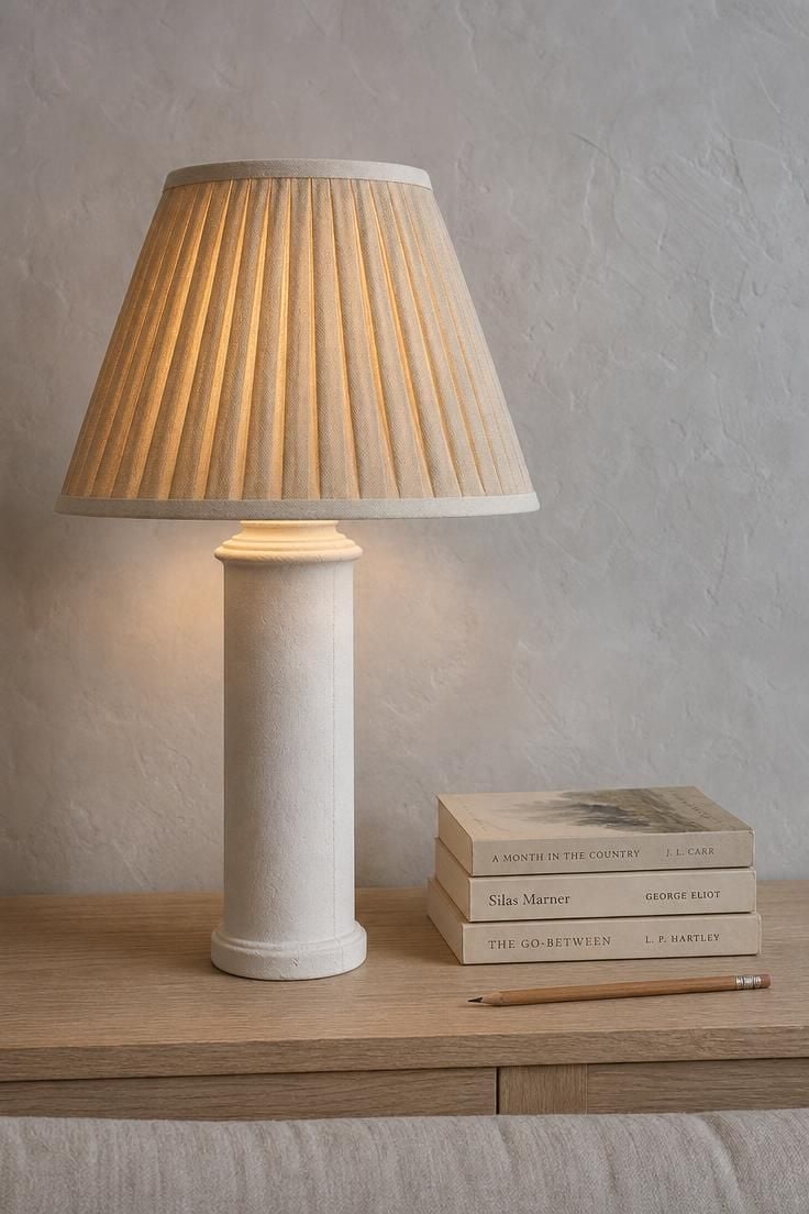13 Breezy Summer Living Room Decor Ideas for a Calm Home 10 A plaster column lamp with a pleated oat linen shade glowing softly against a chalk plaster wall in cool overcast light.
