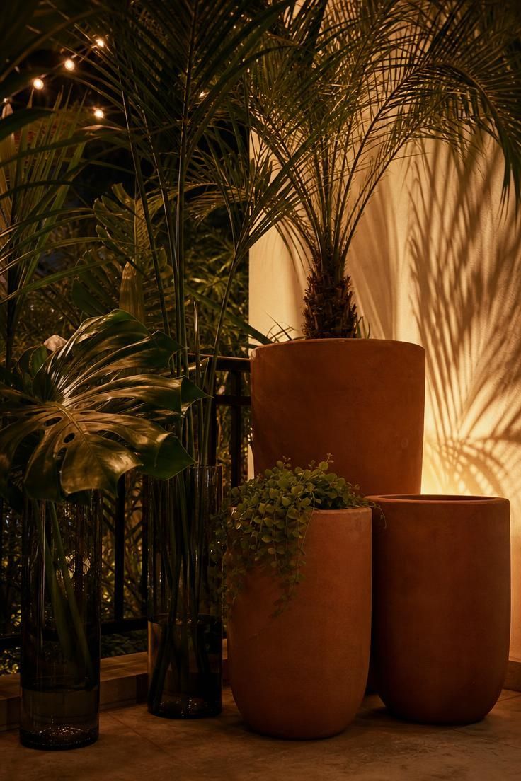 12 Cozy Terrace Decoration Ideas for a Fun Party Night 5 Oversized terracotta planters with palm and monstera leaves in a lush corner, lit by a low uplight casting leaf shadows.
