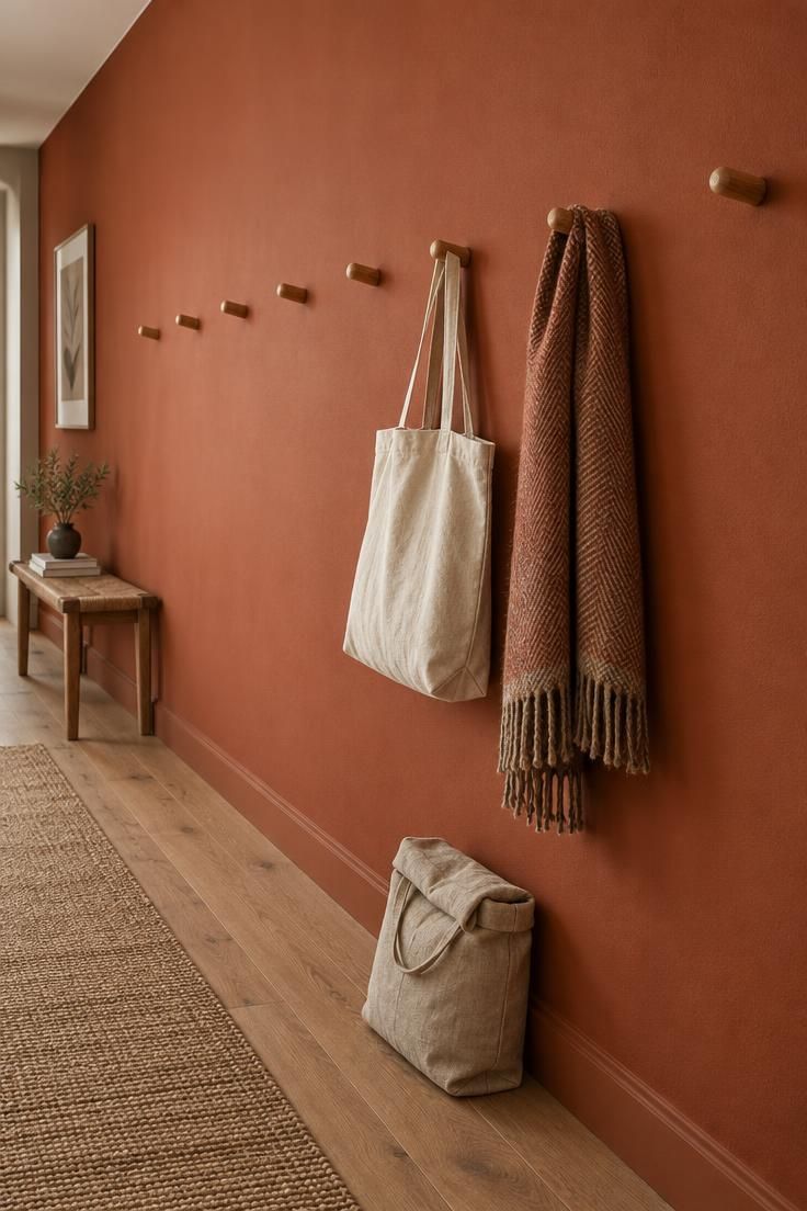 11 Warm Terracotta Hallway Ideas for an Inviting Entry 5 Terracotta accent wall running the length of a hallway with a row of timber hooks, a canvas tote, and a wool scarf hanging against the color.