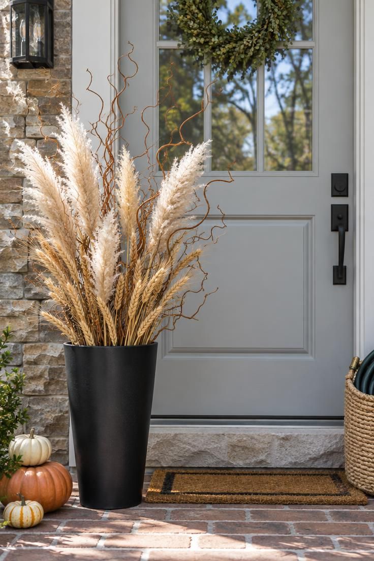11 Warm Thanksgiving Front Door Decor Ideas for a Cozy Entry 9 Light gray front door with a tall black metal planter holding dried pampas grass, wheat stalks, and curly willow on a brick porch.