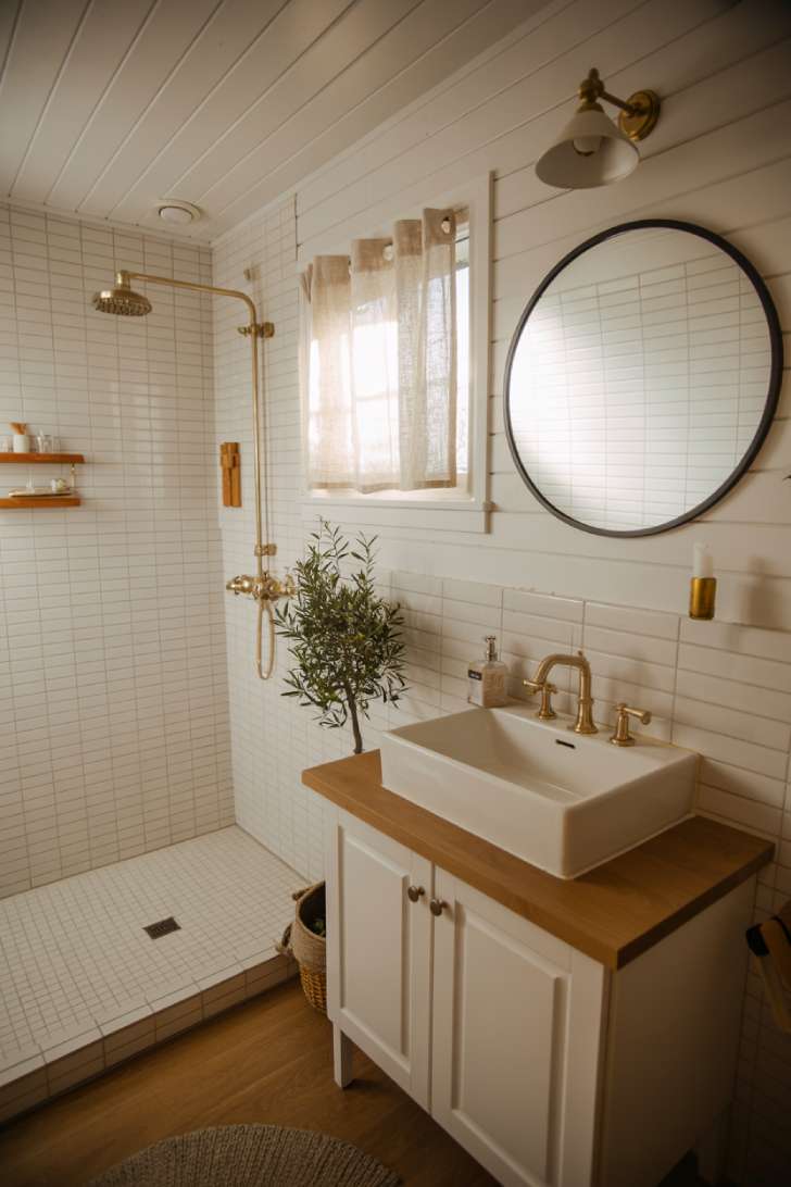 13 Smart Tiny House Bathroom Ideas for Tiny Budgets 12 All-white Scandinavian tiny house bathroom with brass fixtures and oak vanity