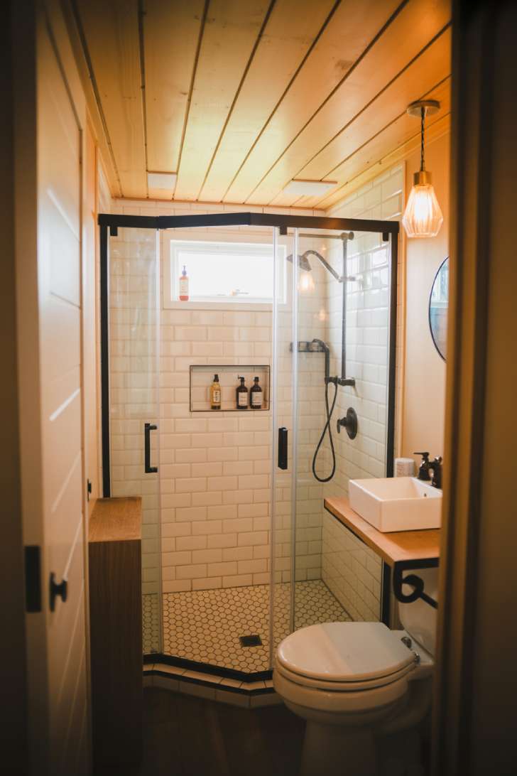 13 Smart Tiny House Bathroom Ideas for Tiny Budgets 2 Frameless glass corner shower in a tiny home bathroom with black fixtures