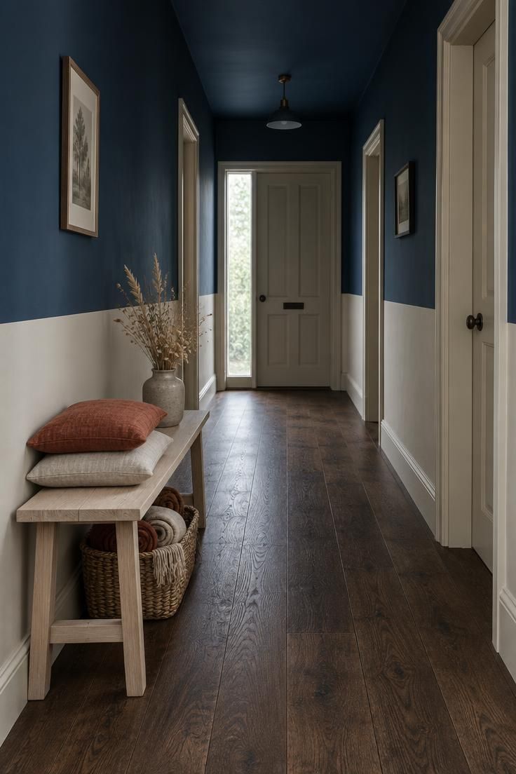 11 Warm Two Tone Hallway Ideas for Small Entryways 2 Hallway with deep ink-blue upper walls above a chalky putty lower band, dark oak floor, pale ash bench with cushions, and diffused daylight from a far glazed door.