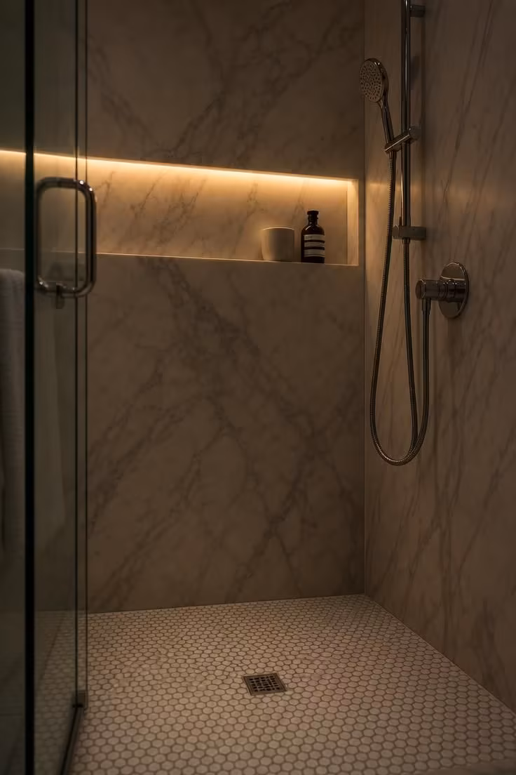 13 Cozy Very Small Bathroom Ideas With Shower Worth Trying 5 Close-up interior of a very small bathroom shower with honed Calacatta marble slab walls, penny round mosaic floor tiles, and a recessed niche lit by a warm LED strip.