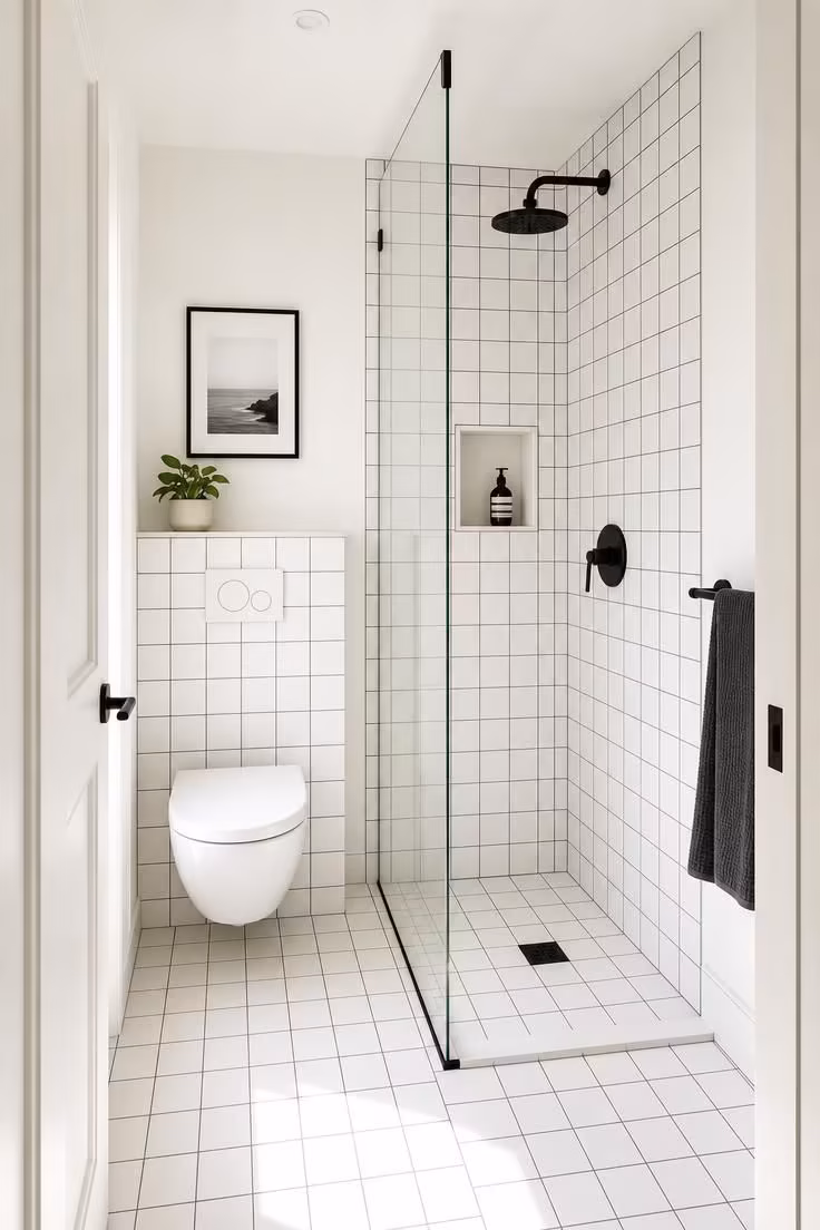 13 Cozy Very Small Bathroom Ideas With Shower Worth Trying 8 A very small bathroom with white 6x6 square tile and charcoal grout on walls and floor, matte black fixtures, and a frameless glass shower panel in bright midday light.