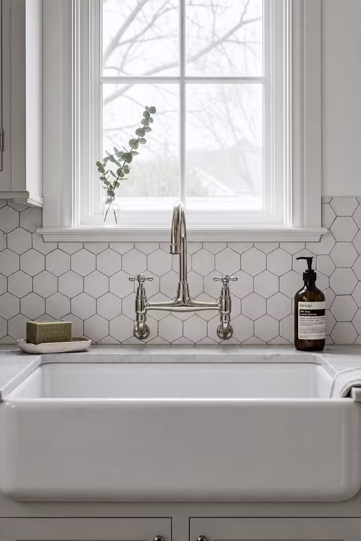 Hand-cut hex tile backsplash in matte white behind a polished nickel bridge faucet in a vintage cottage kitchen