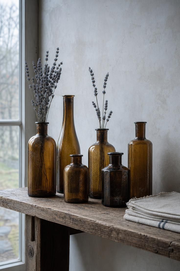 15 Vintage Fall Decor Ideas With Old-World Autumn Charm 8 A cluster of brown-tinted apothecary bottles in varying heights on a reclaimed wood console, some holding dried lavender stems, in cool overcast light.