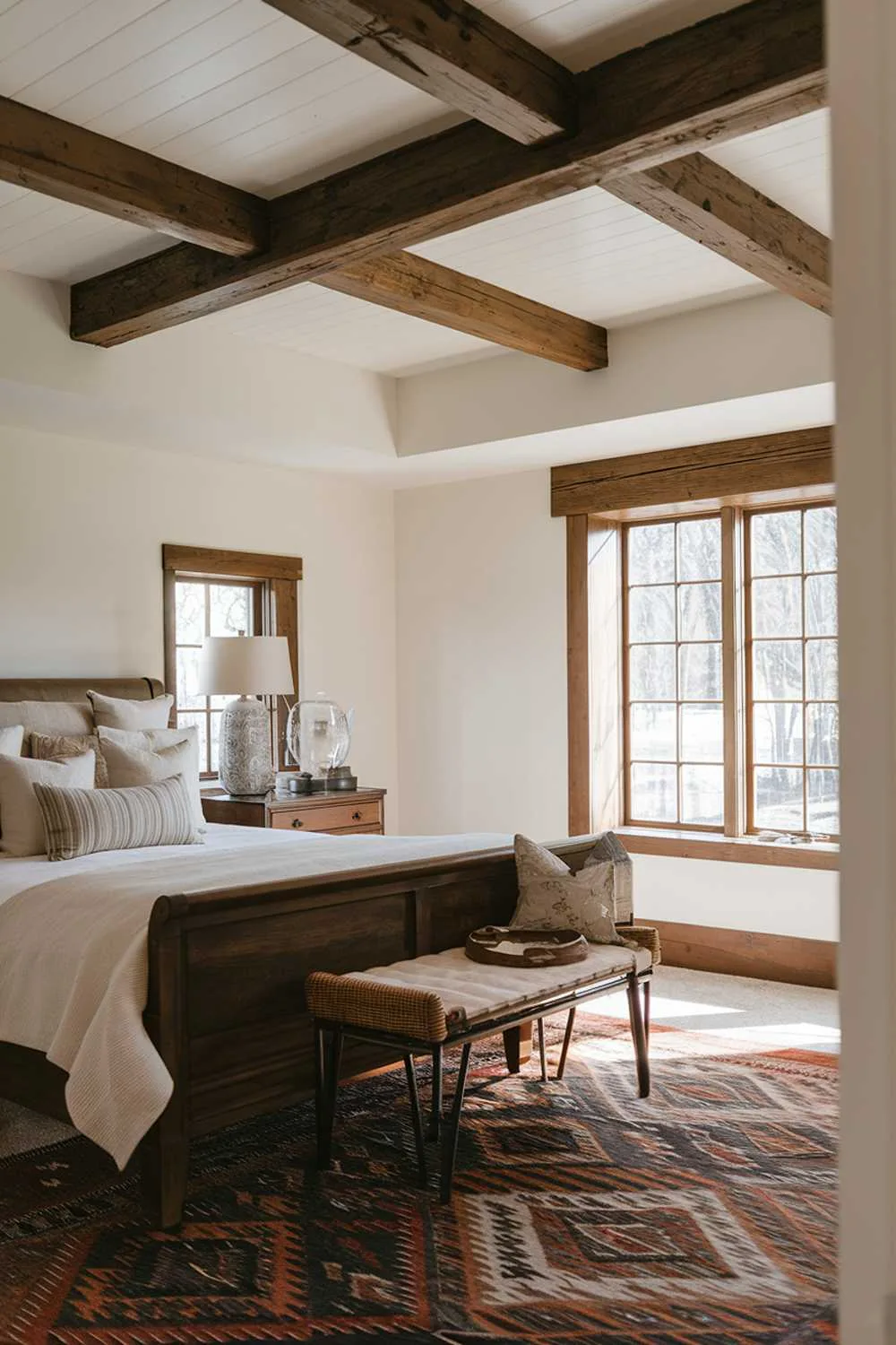 23 Vintage Farmhouse Bedroom Ideas for Cozy Charm 1 Cozy farmhouse bedroom featuring wooden beam ceiling, white walls, and stylish patterned rug with natural light