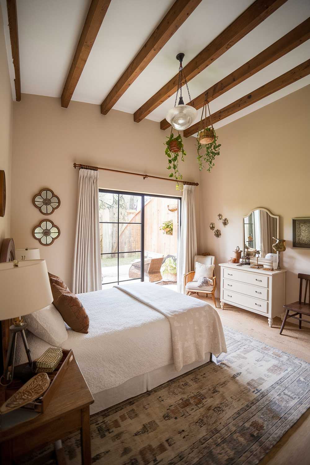 Spacious bedroom with sliding glass door, wooden beams, and hanging plants creating natural flow