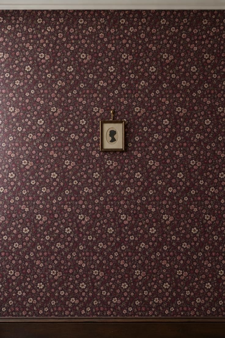 13 Vintage Hallway Looks for a Plain, Unfinished Wall 2 Hallway wall covered in dense small-scale floral wallpaper in deep plum and oxblood with cream and pink blossoms, a dark wood baseboard, and a single small framed silhouette.