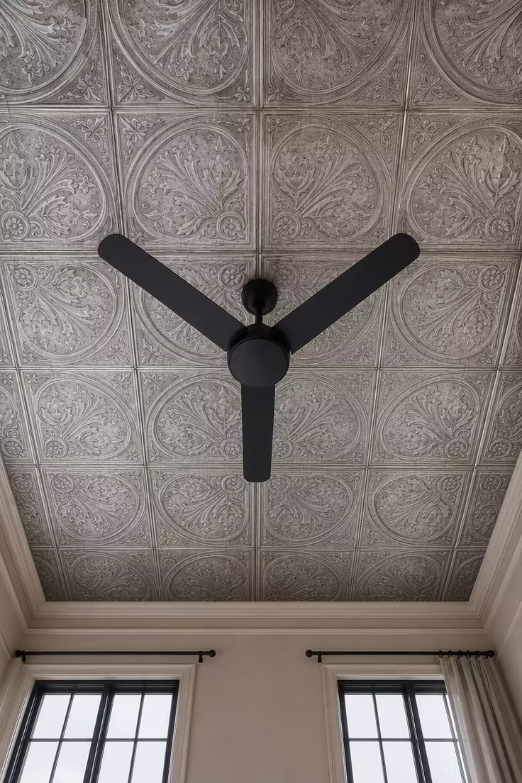 Pressed tin ceiling tiles with aged silver patina surrounding a matte black ceiling fan in cool overcast daylight.