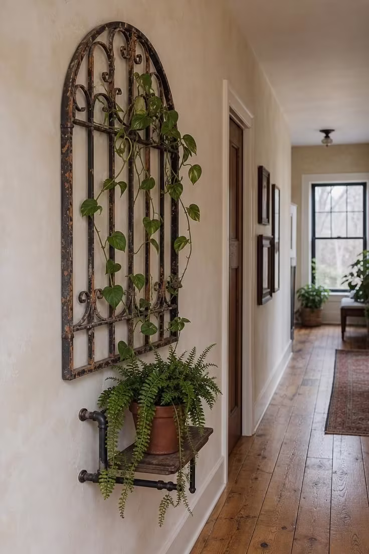 A salvaged wrought iron garden gate mounted on a plaster wall as a trellis with trailing pothos in cool overcast light.
