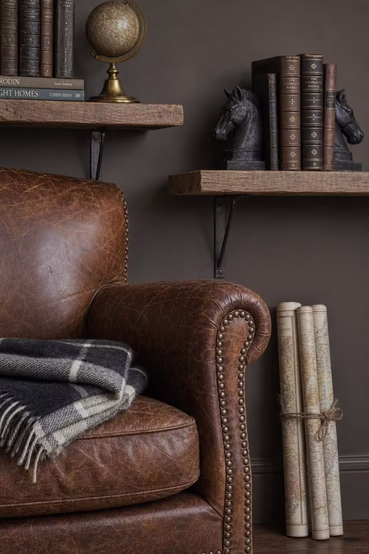 11 Charming Vintage Reading Nook Ideas You Will Love 4 Close-up of a worn brown leather club chair with brass nail heads flanked by reclaimed barn wood shelves holding books and a brass globe