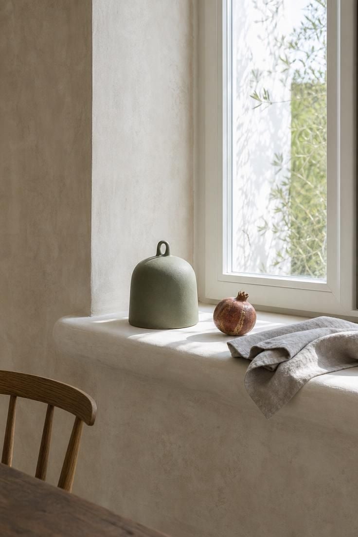 13 Earthy Wabi Sabi Dining Area Ideas That Feel Like Home 7 A deep poured plaster windowsill displaying a ceramic pendant light sample, dried pomegranate, and folded linen napkin in bright midday light.