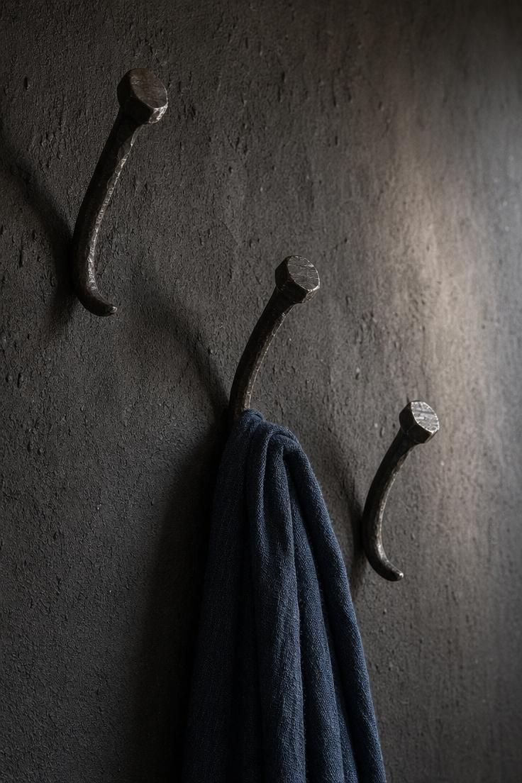 Hand-forged iron nail hooks on a charcoal plaster wall holding a linen scarf in a moody wabi sabi entryway.