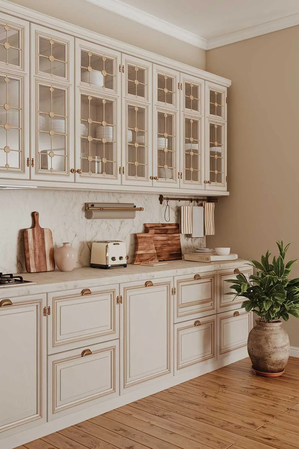 19 Warm Minimalist Kitchen Ideas to Create a Cozy Space 14 A warm minimalist kitchen design and decor. The kitchen has a wooden floor and white cabinets with brass hardware. There is a marble countertop with a toaster, a vase, and a wooden cutting board. A potted plant sits on the floor. The walls are painted beige.