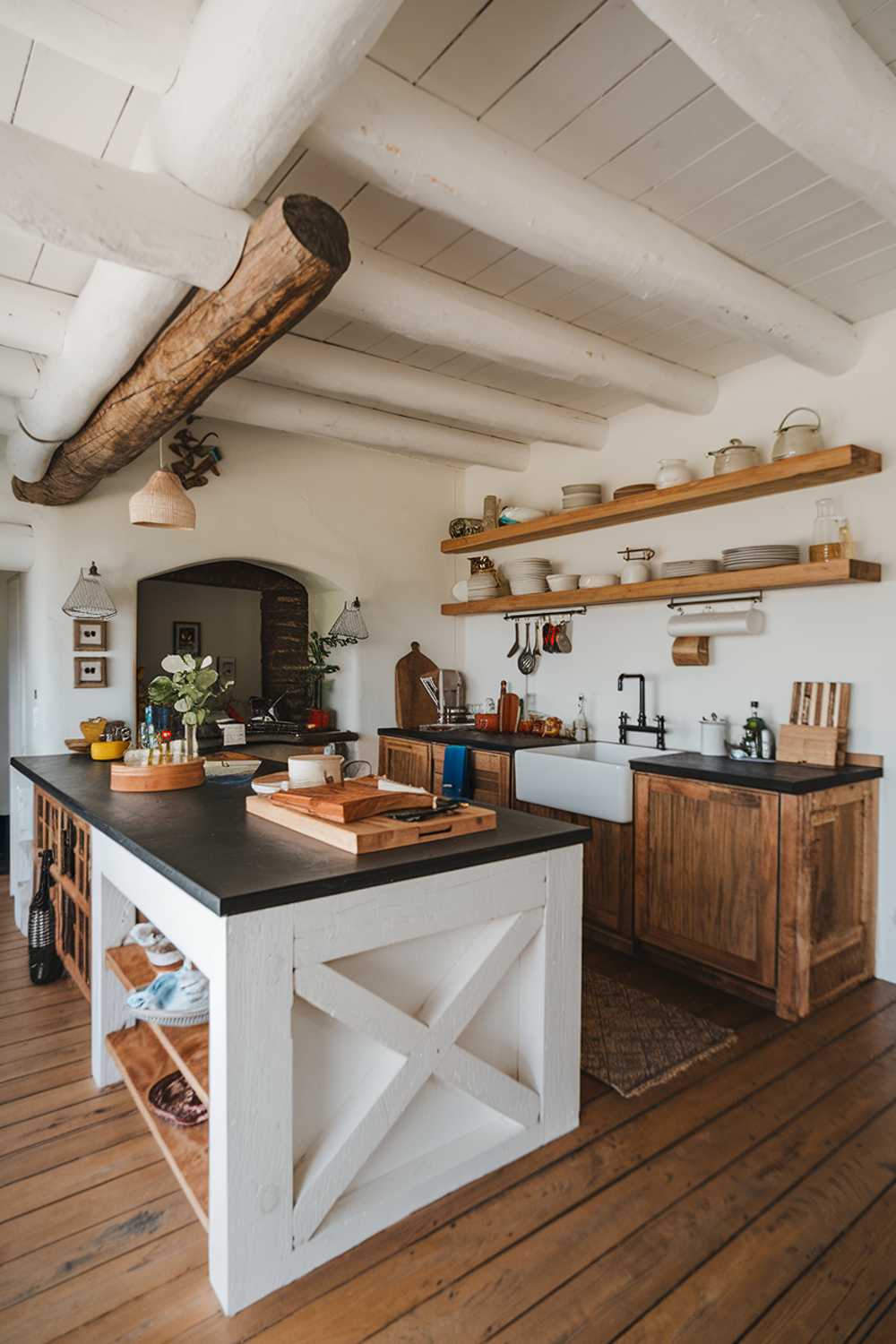 A white and wood kitchen with a rustic decor. The kitchen has a large island with a black countertop and a white sink. There are wooden shelves on the wall, holding various kitchen items. The floor is made of wood. The overall ambiance is warm and inviting.