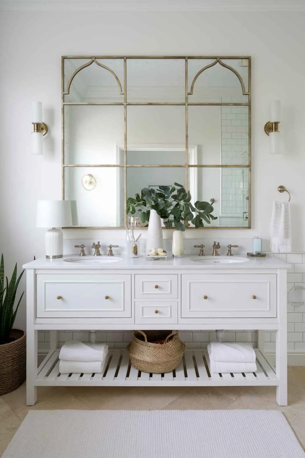 17 White Bathroom Ideas for a Fresh, Stylish Space 5 White bathroom featuring double-sink vanity with large gold-framed mirror, decorative items, white rug, and plant accent