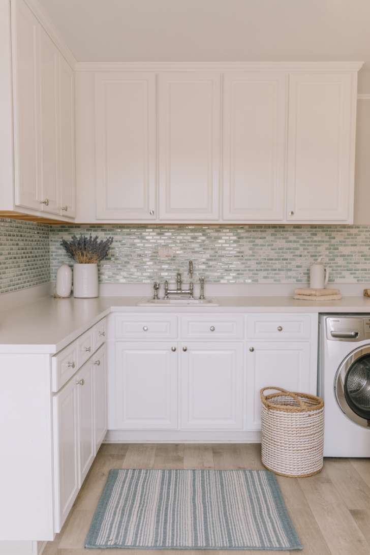 White laundry room with a soft blue mosaic tile backsplash, striped cotton rug, and coastal-inspired accents
